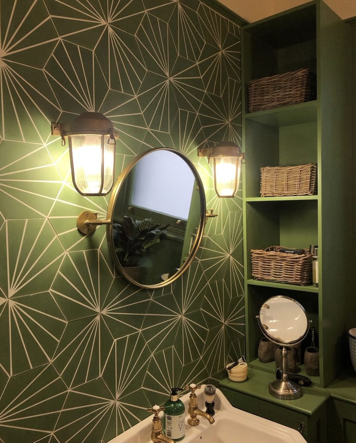 Brass bulkhead wall lights either side of a mirror in a green tiled cloakroom