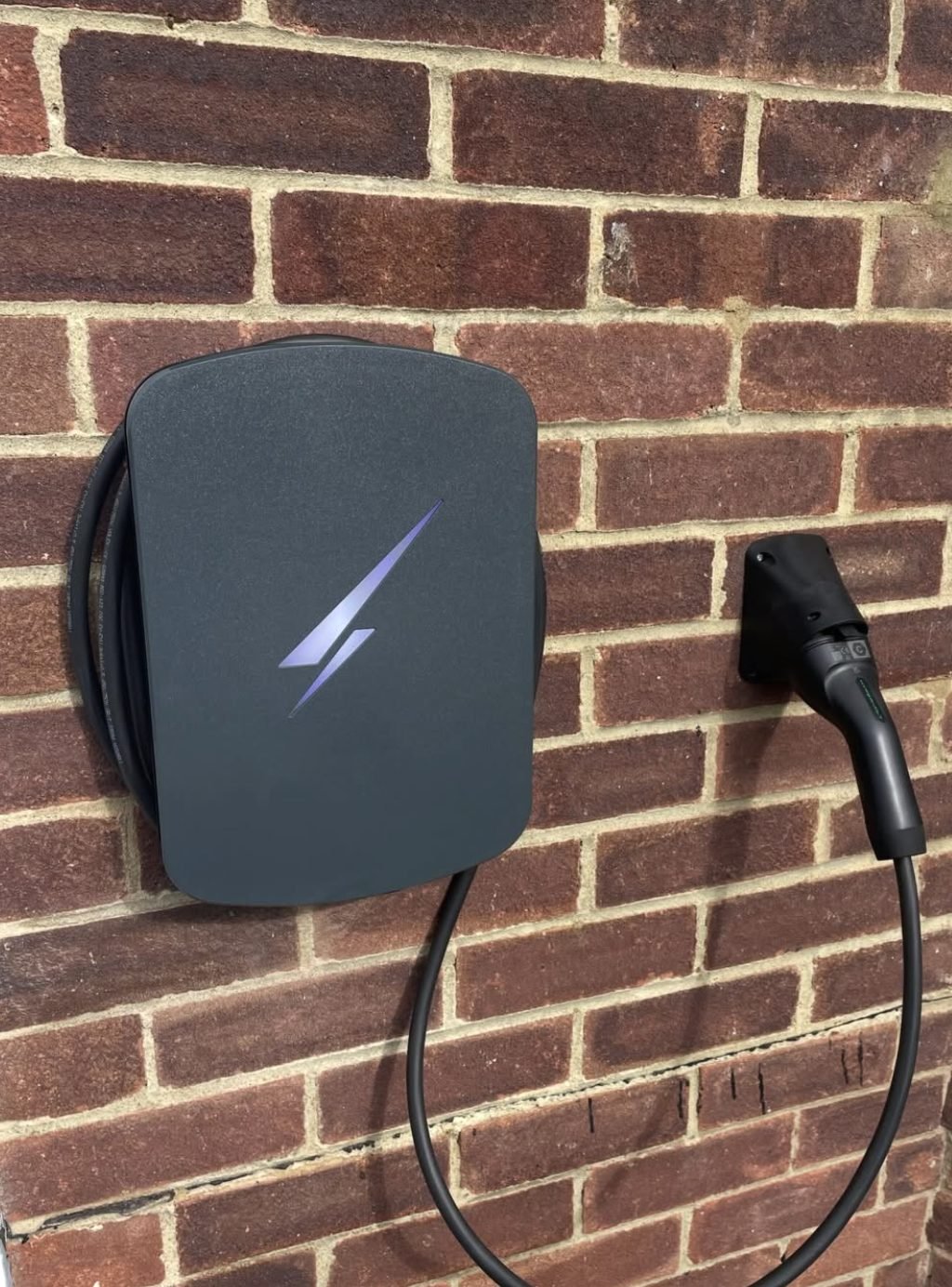 Tethered EV charge point with its lead coiled on a brick wall